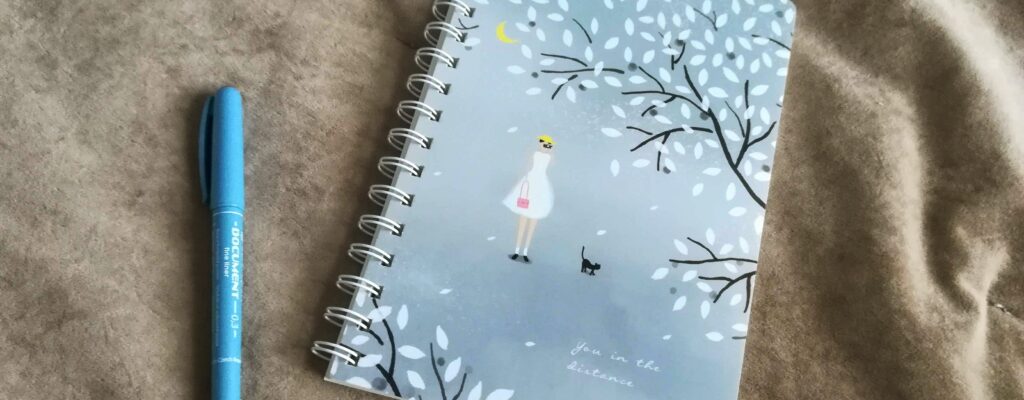 Tužka a zavřený notes s obrázkem dívky a kočičky